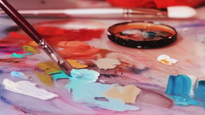 paintbrush with teal paint pressed to a pallet with orange red tan pink paint